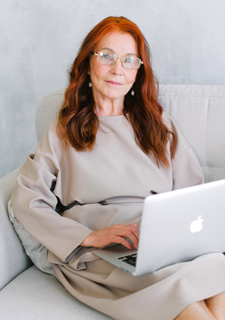 Femme assise sur un canapé blanc travaillant sur son macbook